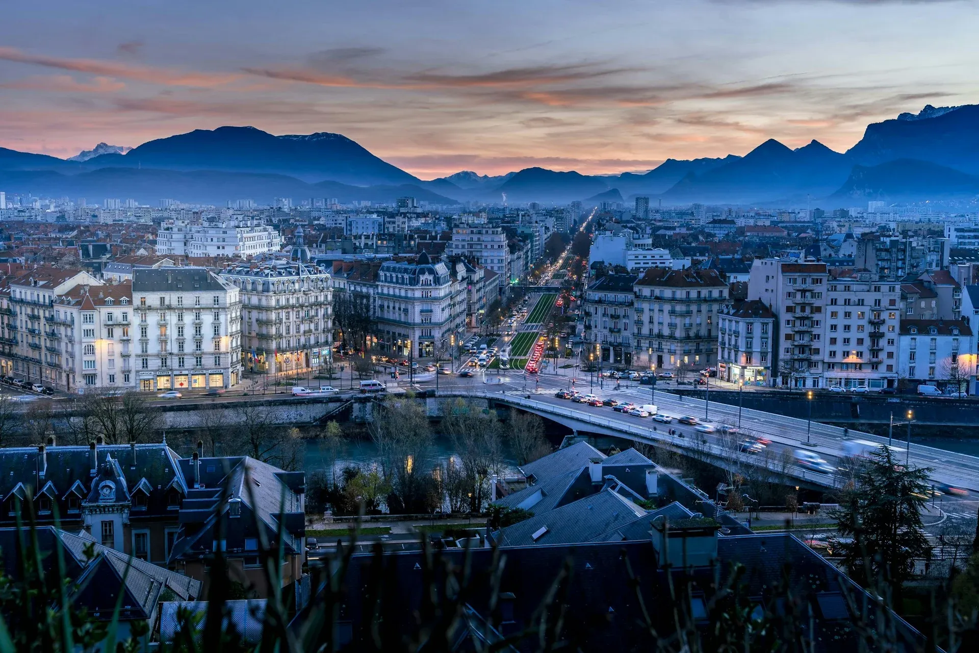 Vista panorâmica de Grenoble, França, ao entardecer, com luzes da cidade e montanhas ao fundo