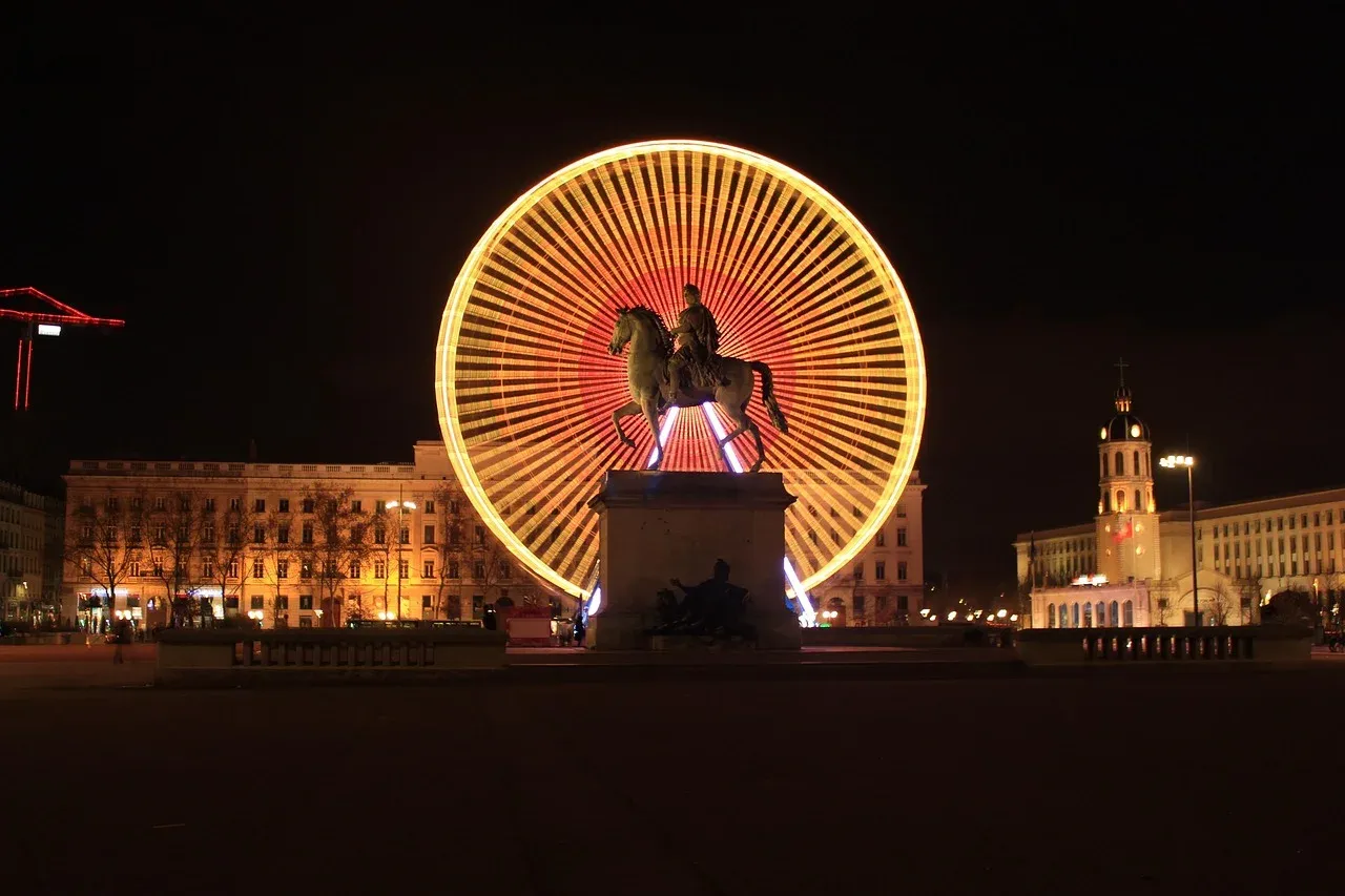 Estátua de Luís XIV na Place Bellecour em Lyon à noite, com uma roda-gigante iluminada ao fundo