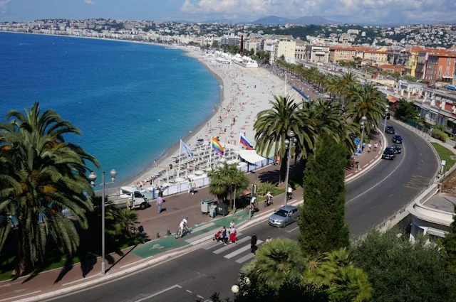  Nice, France featuring the curved Promenade des Anglais alongside the azure Mediterranean sea, a busy beach and cityscape.