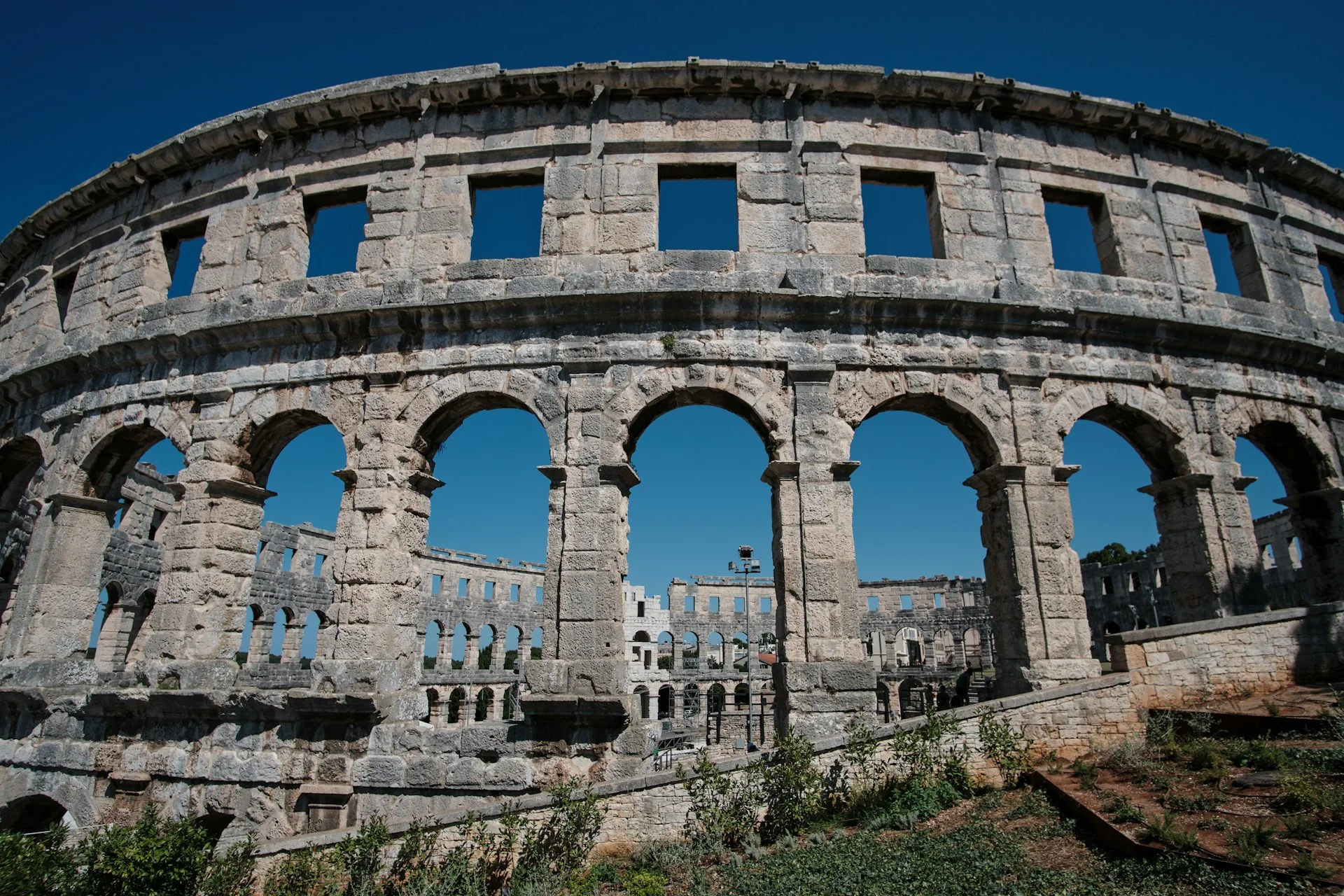 Pula Arena, Croatia: ancient Roman amphitheatre highlighting its well preserved arches and stone facade against a clear blue sky